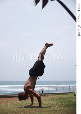 Man holding handstand on grass near ocean in tropical setting Man holding handstand on grass near ocean in tropical setting 138001591