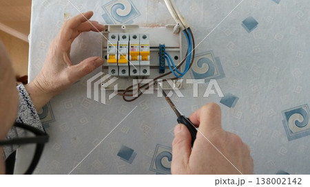 Male hands holding a screwdriver and adjusting the operation of a home electric meter hanging on a wall with old wallpaper, a man repairing and installing an electric meter on a room wall Male hands holding a screwdriver and adjusting the operation of a home electric meter hanging on a wall with old wallpaper, a man repairing and installing an electric meter on a room wall 138002142