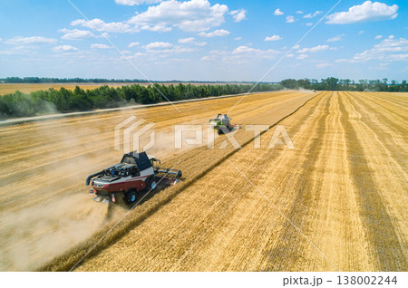 Aerial view of combine harvesters harvesting wheat in a field on a sunny day 138002244