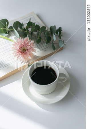 白いカップのホットコーヒーと本と花 日差しの入る朝のテーブル ナチュラルでやさしいリラックスタイム 138002846