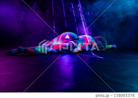 Woman with vibrant fluorescent body paint lying in dark studio with neon lights and smoke. 138003378