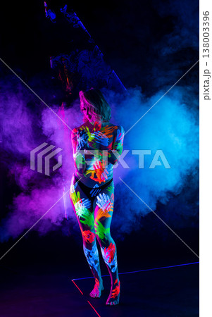 Woman with fluorescent handprint body art posing in vibrant ultraviolet light and colorful smoke. Woman with fluorescent handprint body art posing in vibrant ultraviolet light and colorful smoke. 138003396