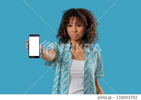 Smiling african teen woman showing smartphone white screen on blue. Mock-up Smiling african teen woman showing smartphone white screen on blue. Mock-up 138003702