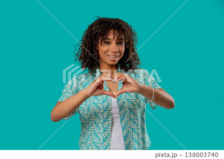 Pretty woman forms heart shape with hands, sending love. Charming teenage girl on blue background. Women health, volunteering, charity donation, gratitude symbol, flirting Pretty woman forms heart shape with hands, sending love. Charming teenage girl on blue background. Women health, volunteering, charity donation, gratitude symbol, flirting 138003740
