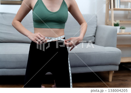 young woman wearing exercise clothes taking a waist measurement 138004205