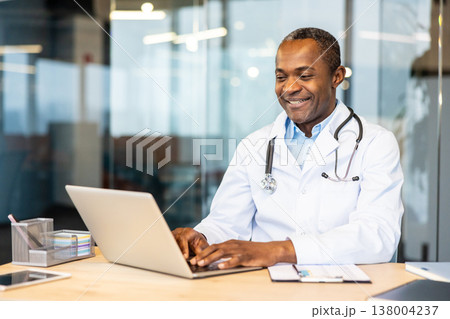 Experienced physician wearing a lab coat and stethoscope, smiling and typing on a laptop at a modern office desk, actively engaging in telehealth and digital healthcare services Experienced physician wearing a lab coat and stethoscope, smiling and typing on a laptop at a modern office desk, actively engaging in telehealth and digital healthcare services 138004237