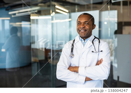 Medical doctor wearing a lab coat and stethoscope, standing with arms crossed and smiling confidently, representing healthcare expertise and professional service in a modern clinic environment Medical doctor wearing a lab coat and stethoscope, standing with arms crossed and smiling confidently, representing healthcare expertise and professional service in a modern clinic environment 138004247