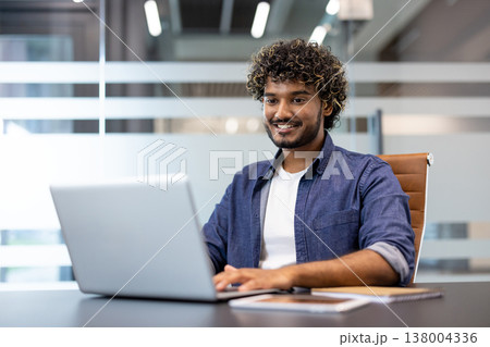 Portrait of a young Muslim man sitting in the office at a desk and working on a laptop. 138004336