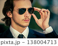 Closeup portrait of  a male fashion model with sunglasses in a stylish blue suit with tie. Handsome young man model in elegant business suit poses with sunglasses. 138004713
