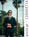 Stylish portrait of  a male fashion model with sunglasses in a elegance blue suit with tie. Handsome young man model in modern business suit poses with sunglasses posing in the street. 138004714
