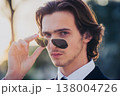 attractive man has lowered his sunglasses on his nose and is looking into the camera  138004726
