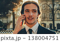 Smiling businessman in the city talking on a cell phone. Portrait Businessman in a business suit in the the street a with mobile phone. Young man in a business  suit talking on a smartphone. 138004751