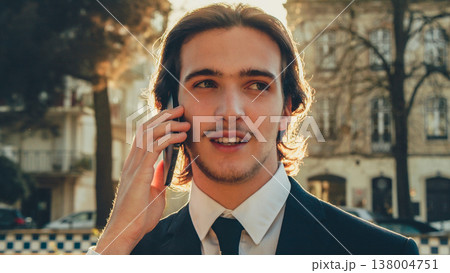 Smiling businessman in the city talking on a cell phone. Portrait Businessman in a business suit in the the street a with mobile phone. Young man in a business suit talking on a smartphone. Smiling businessman in the city talking on a cell phone. Portrait Businessman in a business suit in the the street a with mobile phone. Young man in a business suit talking on a smartphone. 138004751