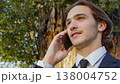 Portrait of the  Businessman in a business suit in the park  with mobile phone.  Smiling businessman talking on a cell phone., outdoors. Young man in a business  suit talking on a smartphone in nature 138004752