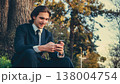 Happy man in a business suit sets outdoors and using a smartphone. Portrait of the young man in a business suit with mobile phone, in the park. Smiling businessman in city looking to a cell phone. 138004754