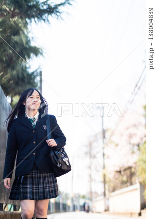 春の通学路を笑顔で歩く女子高校生。桜が咲き始める中、新しい季節を迎える学生の登校シーン 138004839