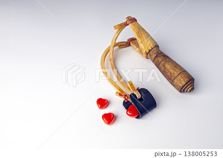 Rustic Handcrafted Wooden Slingshot with Elastic Bands and Leather Pouch Loaded with Glossy Red Heart-Shaped Candies Symbolizing the Act of Sending Love and Affection on a Clean White Background Rustic Handcrafted Wooden Slingshot with Elastic Bands and Leather Pouch Loaded with Glossy Red Heart-Shaped Candies Symbolizing the Act of Sending Love and Affection on a Clean White Background 138005253