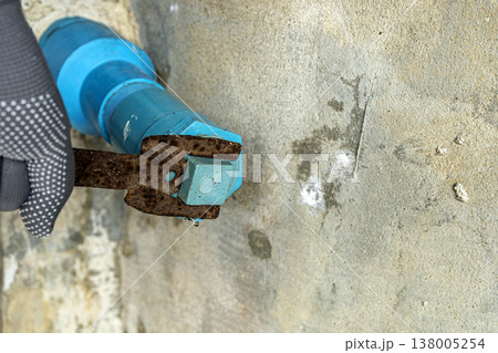 Close-Up of Construction Worker Wearing Gray Dotted Safety Gloves Using a Heavily Rusted Wrench to Tighten a Blue Hex Bolt on a Rough Concrete Wall During Building Work Close-Up of Construction Worker Wearing Gray Dotted Safety Gloves Using a Heavily Rusted Wrench to Tighten a Blue Hex Bolt on a Rough Concrete Wall During Building Work 138005254