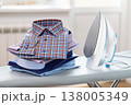 Folded long sleeve shirts and iron on ironing board in room 138005349