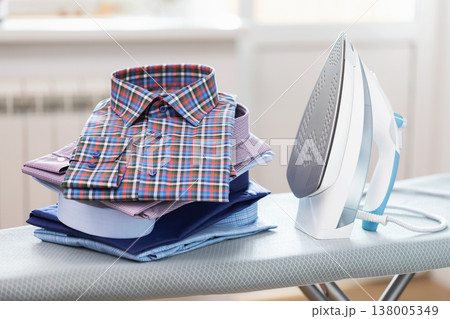 Folded long sleeve shirts and iron on ironing board in room 138005349