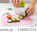 Close-up of the hands of a nine-year-old child cutting cucumber into slices with a ribbed stainless steel knife on a cutting board on a kitchen table 138005354