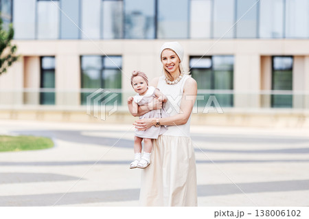 Portrait beautiful young mother with small daughter outdoors in city. Stylish woman and little girl wearing beige summer dresses, modern urban lifestyle, family love, fashion outside Portrait beautiful young mother with small daughter outdoors in city. Stylish woman and little girl wearing beige summer dresses, modern urban lifestyle, family love, fashion outside 138006102