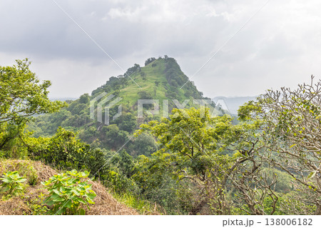 Verdant Tropical Hillside Landscape Under Overcast Sky: Lush Green Foliage and Distant Mountains Form a Serene Natural Vista. Sri Lanka island in Asia. Verdant Tropical Hillside Landscape Under Overcast Sky: Lush Green Foliage and Distant Mountains Form a Serene Natural Vista. Sri Lanka island in Asia. 138006182