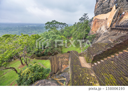 Sigiriya ancient rock fortress in Sri Lanka. Ancient Staircase Carved into a Massive Rock Formation Overlooking Lush Green Forest and Distant Horizon Under Cloudy Sky Sigiriya ancient rock fortress in Sri Lanka. Ancient Staircase Carved into a Massive Rock Formation Overlooking Lush Green Forest and Distant Horizon Under Cloudy Sky 138006193