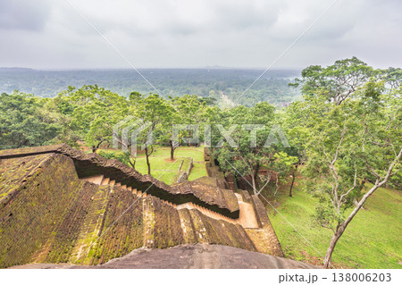Sigiriya ancient rock fortress in Sri Lanka. Ancient Staircase and Garden Complex with Lush Green Forest Landscape Under an Overcast Sky from High Vantage Point 138006203