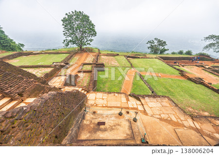 Sigiriya ancient rock fortress in Sri Lanka. Ancient architectural ruins with lush green terraces and a solitary tree under an overcast sky, showcasing historical landscape Sigiriya ancient rock fortress in Sri Lanka. Ancient architectural ruins with lush green terraces and a solitary tree under an overcast sky, showcasing historical landscape 138006204