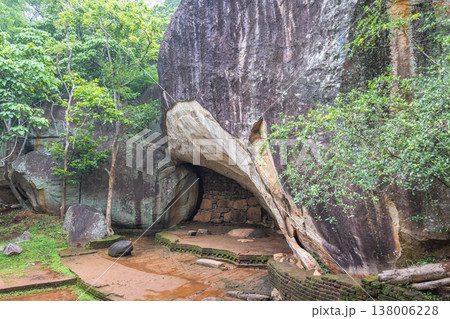 Sigiriya ancient rock fortress in Sri Lanka. Ancient cave shelter formed by massive rock formations amidst lush green jungle foliage and weathered stone paths 138006228