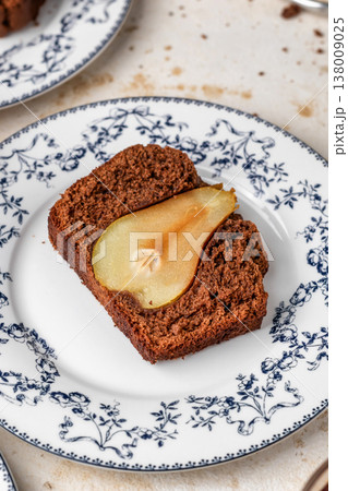 Chocolate cake with pears baked inside. Chocolate pear loaf cake with pear served on ceramic plate on beige textured background. Home cooking recipe 138009025