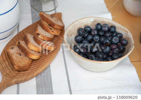 Sugar coated rusks and fresh blueberries in bowl on table in home kitchen with natural light, simple snack composition in everyday domestic setting. Food styling, healthy snack, breakfast, lifestyle Sugar coated rusks and fresh blueberries in bowl on table in home kitchen with natural light, simple snack composition in everyday domestic setting. Food styling, healthy snack, breakfast, lifestyle 138009620