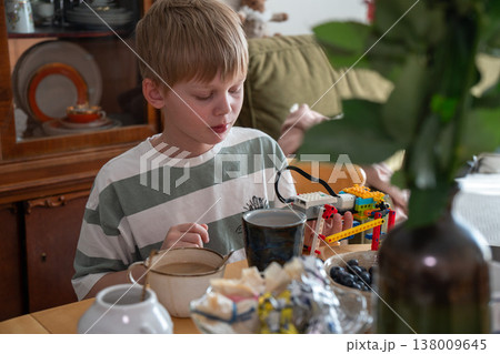 Boy sits at table with construction toy and cup in home interior with natural light and everyday setting, focused activity and learning moment. Childhood activity, education content, creativity 138009645