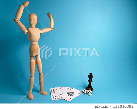 Wooden figure stands with raised arms near playing cards and a chess piece on a blue background Wooden figure stands with raised arms near playing cards and a chess piece on a blue background 138010392