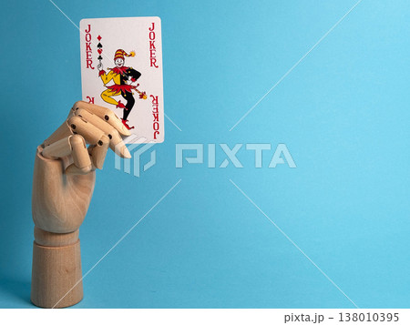 Wooden hand holds a joker playing card against a blue background in a simple setup 138010395