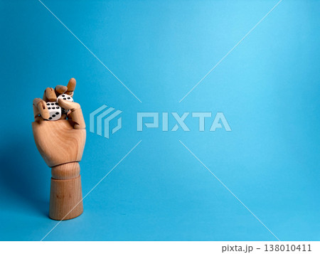 Wooden hand holds two dice against a bright blue background in a playful display of chance and games Wooden hand holds two dice against a bright blue background in a playful display of chance and games 138010411