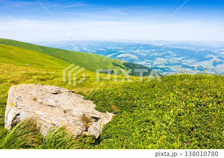 rock on the edge of the mountain meadow in summer. green alpine scenery with boulder on a sunny day. scenic view of carpathian mountains under blue sky. rolling landscape with hills and meadows 138010780