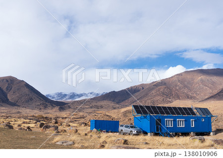 Blue shipping container house with solar panels in a remote mountain landscape. Off-grid living concept with a pickup truck parked next to an alternative cabin. Sustainable energy base camp Blue shipping container house with solar panels in a remote mountain landscape. Off-grid living concept with a pickup truck parked next to an alternative cabin. Sustainable energy base camp 138010906