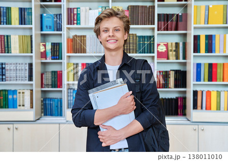 Portrait of smiling teenage student with backpack textbooks in classroom library Portrait of smiling teenage student with backpack textbooks in classroom library 138011010