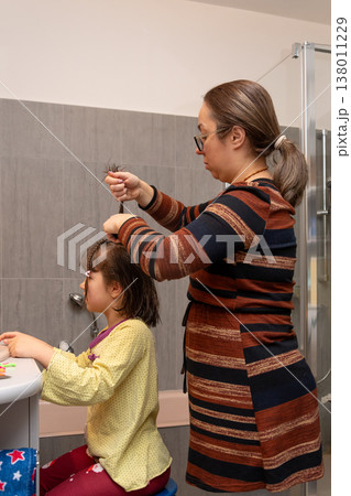Mother gathers and braids her daughter's hair after washing in a modern bathroom. Mother gathers and braids her daughter's hair after washing in a modern bathroom. 138011229