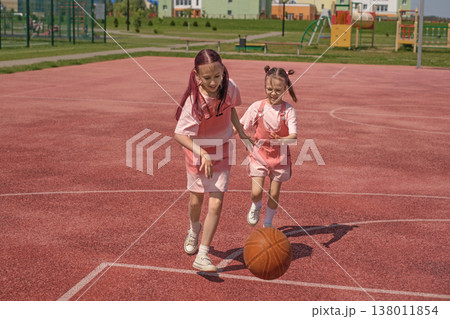Girls play basketball on an outdoor basketball court on a hot summer vacation day. The red rubber covering of the sports field. Healthy sports education 138011854