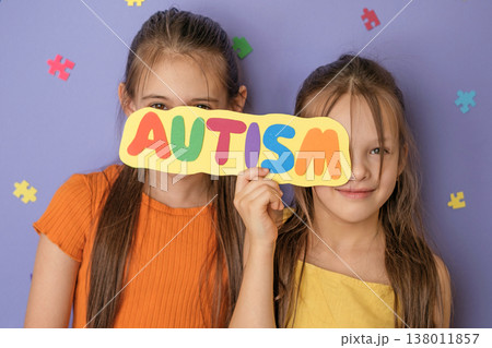Beautiful girls hide their faces behind a card labeled autism. Support for organizations and initiatives to protect the rights and well-being of people with autism Beautiful girls hide their faces behind a card labeled autism. Support for organizations and initiatives to protect the rights and well-being of people with autism 138011857