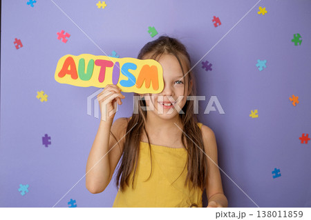 A happy little laughing girl shows a multicolored letter card with the word autism. Awareness and support for people with autism spectrum disorder. 138011859