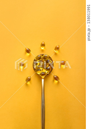 Golden spoon with soft gels vitamin D (cholecalciferol) in shape of sun 138011991