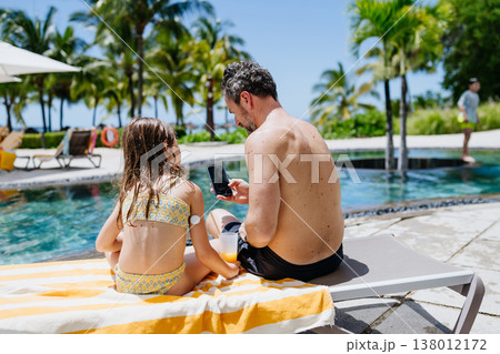 Family relaxing by tropical resort pool, child with diabetes wears glucose monitor. 138012172