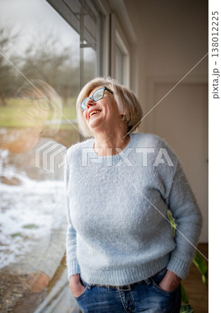 Smiling elderly woman looking through window at home. 138012225
