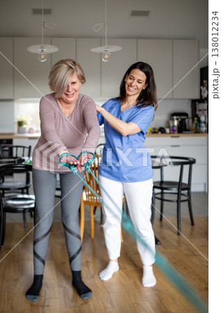 Physiotherapist guiding senior woman during resistance band exercise. Physiotherapist guiding senior woman during resistance band exercise. 138012234