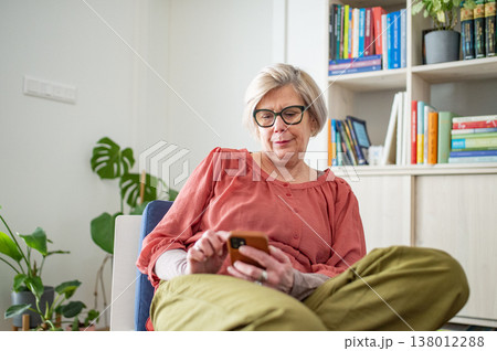 Older woman scrolling on phone while working from home during retirement. Older woman scrolling on phone while working from home during retirement. 138012288