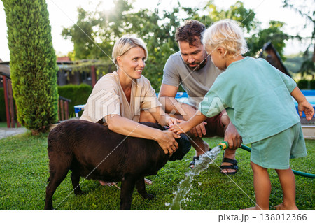 Parents and child cooling dog with water on sunny day. 138012366